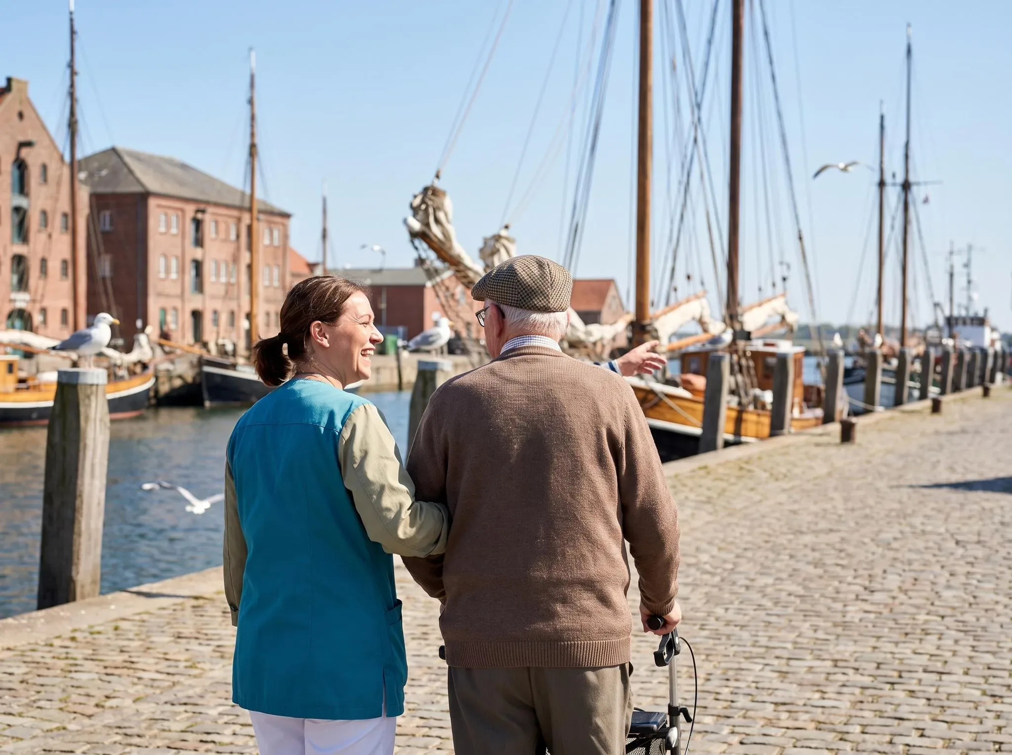 Betreuungskraft und älterer Herr mit Rollator beim Spaziergang am Museumshafen Greifswald