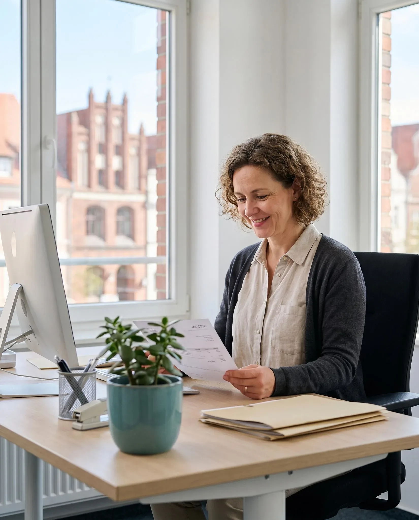 Mitarbeiterin der Buchhaltung prüft lächelnd eine Rechnung, hinter ihr Backsteingiebel der Altstadt